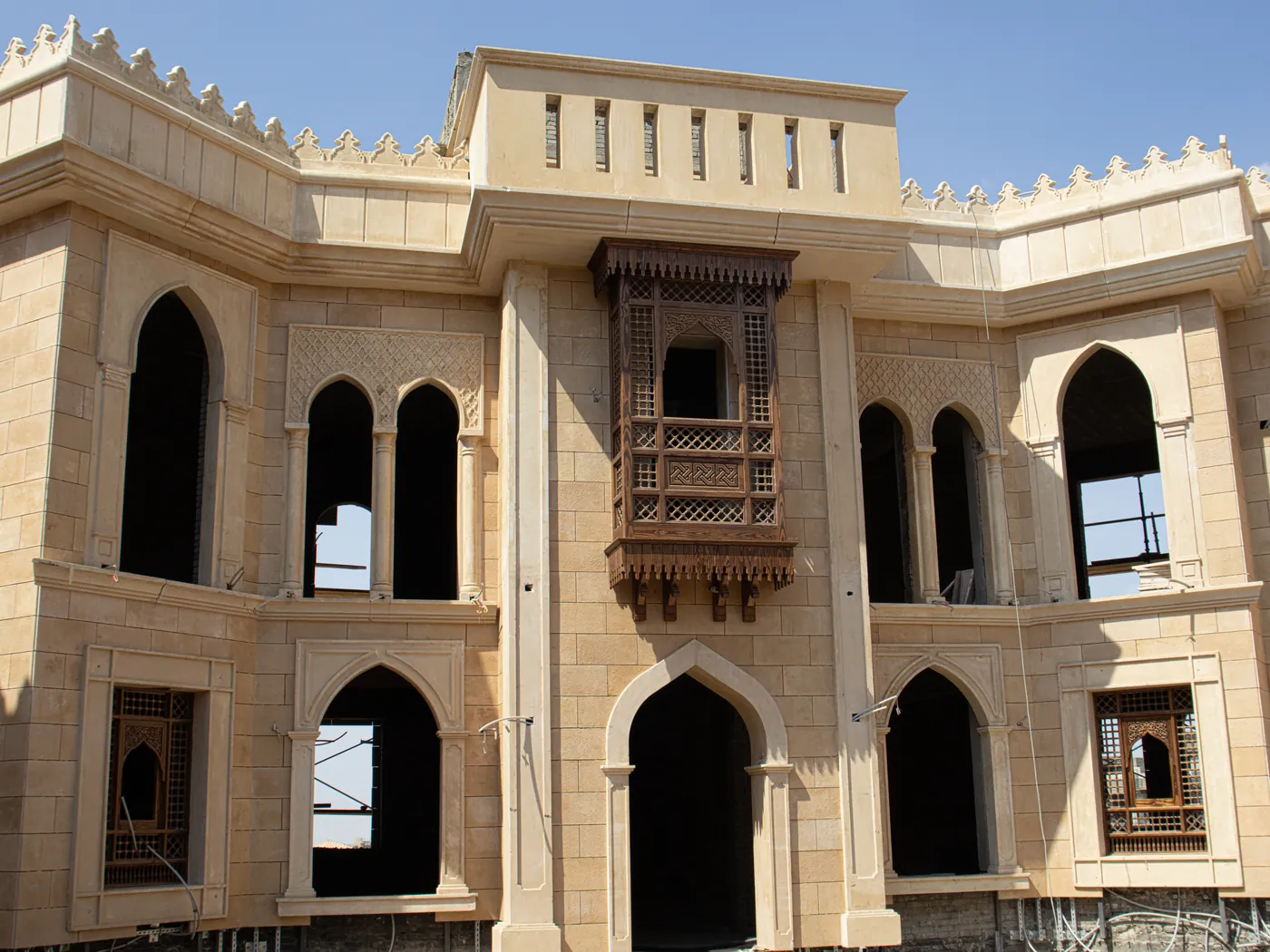Al Buhar City — clad courtyard elevation with pointed arches, a carved mashrabiya oriel and a crenellated parapet